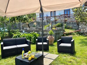 Un espacio al aire libre con mobiliario de mimbre y una mesa dispuesta con frutas y una botella.