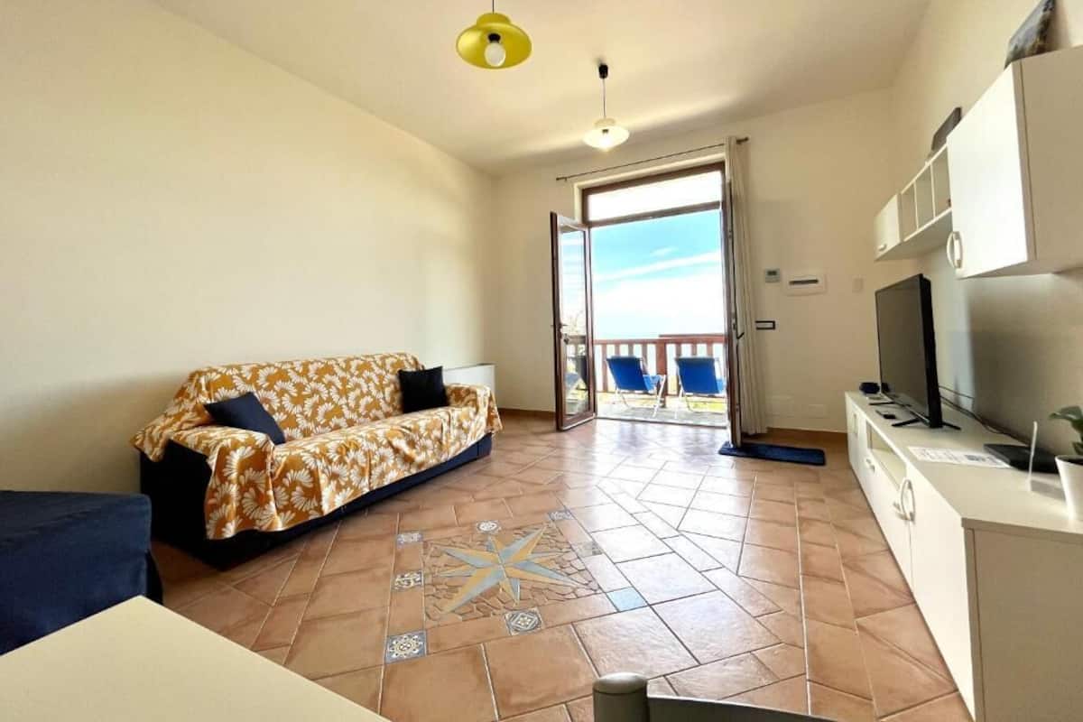 A living room with a sofa, a television, and a kitchen area.