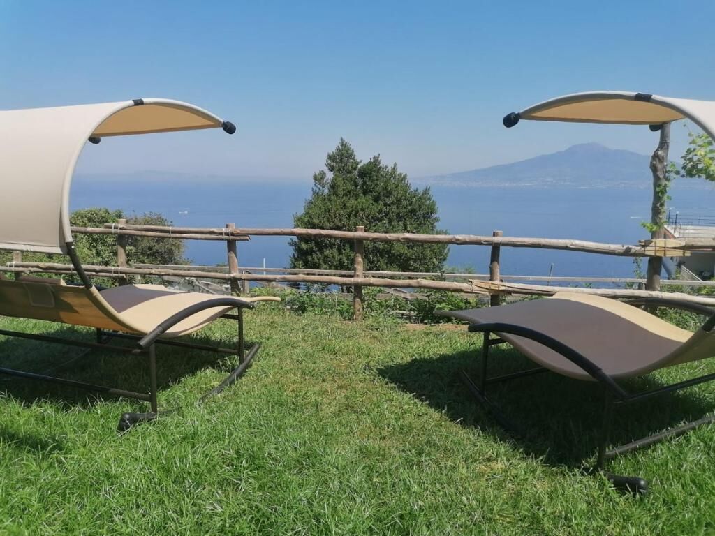 Two outdoor chairs with canopies, a wooden fence, and a view of the sea and mountains.