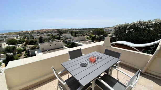 Une terrasse sur le toit, avec une table et des chaises, d’où l’on a vue sur un quartier résidentiel et la mer.