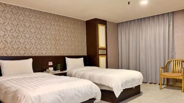 Ein Hotelzimmer mit zwei Betten, einem Nachttisch, einem Sessel und einer Wand mit Muster.