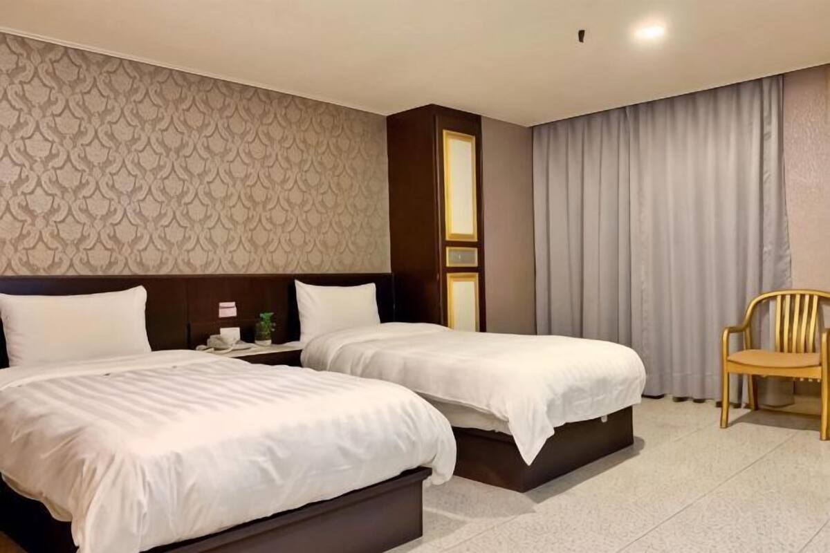 Ein Hotelzimmer mit zwei Betten, einem Nachttisch, einem Sessel und einer Wand mit Muster.