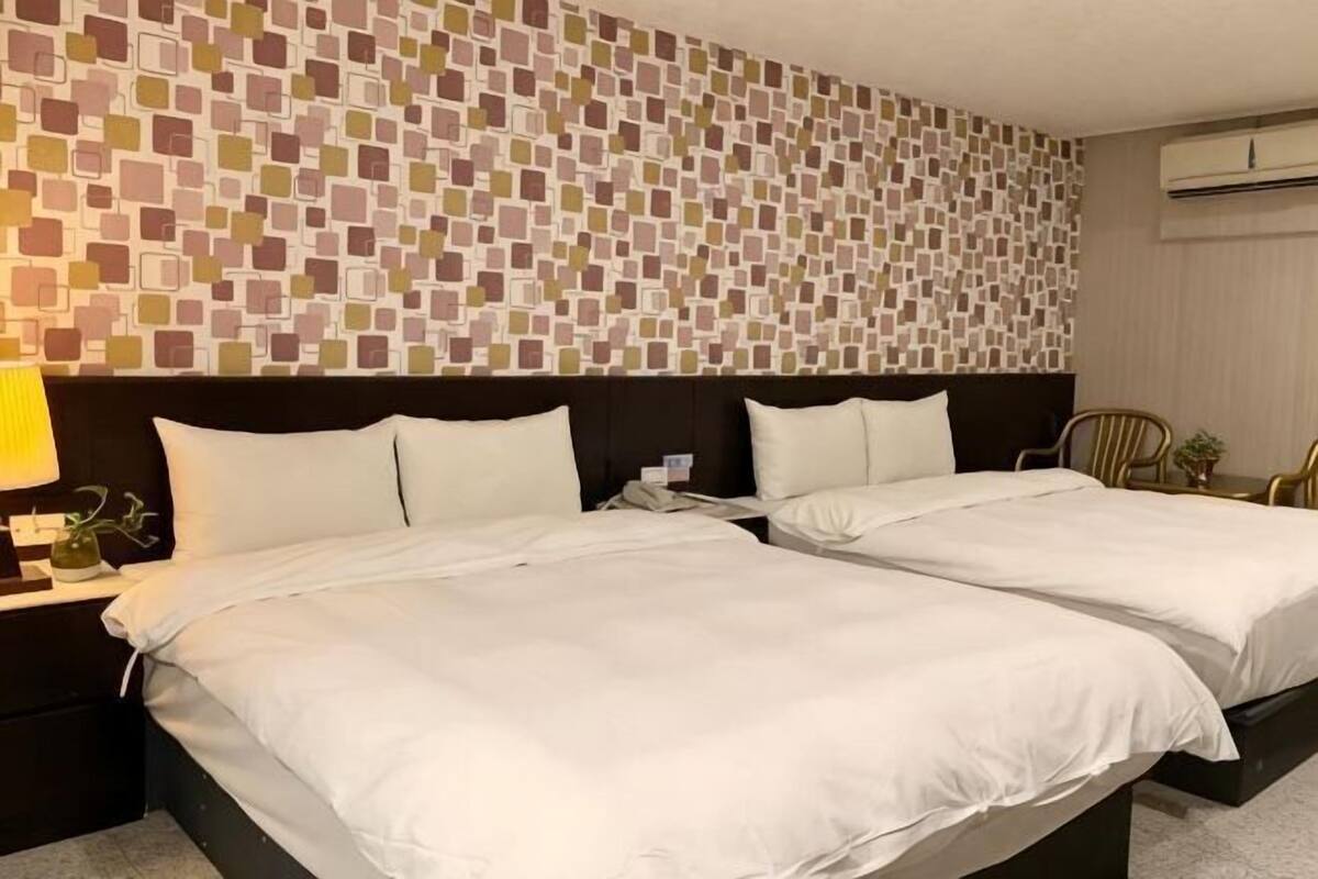 Ein Hotelzimmer mit zwei Betten, einer Wand mit Muster, einem Nachttisch mit Lampe und einem Sessel.