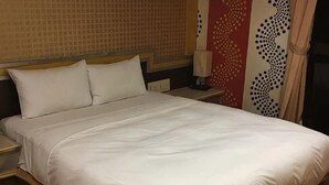 Ein ordentlich bezogenes Bett mit weißen Leinen, einem Kopfteil und einem Nachttisch mit Lampe.