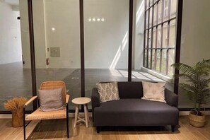 A modern interior with a sofa, chair, and small table, large windows, and a potted plant. - Chju Inn (Tainan)