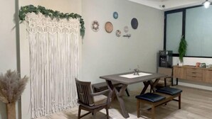 A dining area with a wooden table, two chairs, a macrame wall hanging, and a plant. - Chju Inn (Tainan)