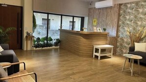 A reception area with a wooden reception desk, a small white table, and a seating area with a sofa and chairs. - Chju Inn (Tainan)