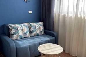 Una habitación con un sofá azul, una mesa redonda y cortinas ligeras.