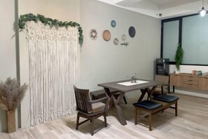 A dining area with a table and chairs, a macrame wall hanging, and a window with a view. - Chju Inn (Tainan)