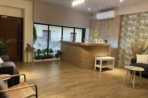 A reception area with a wooden reception desk, seating arrangements, and a view of the outside. - Chju Inn (Tainan)