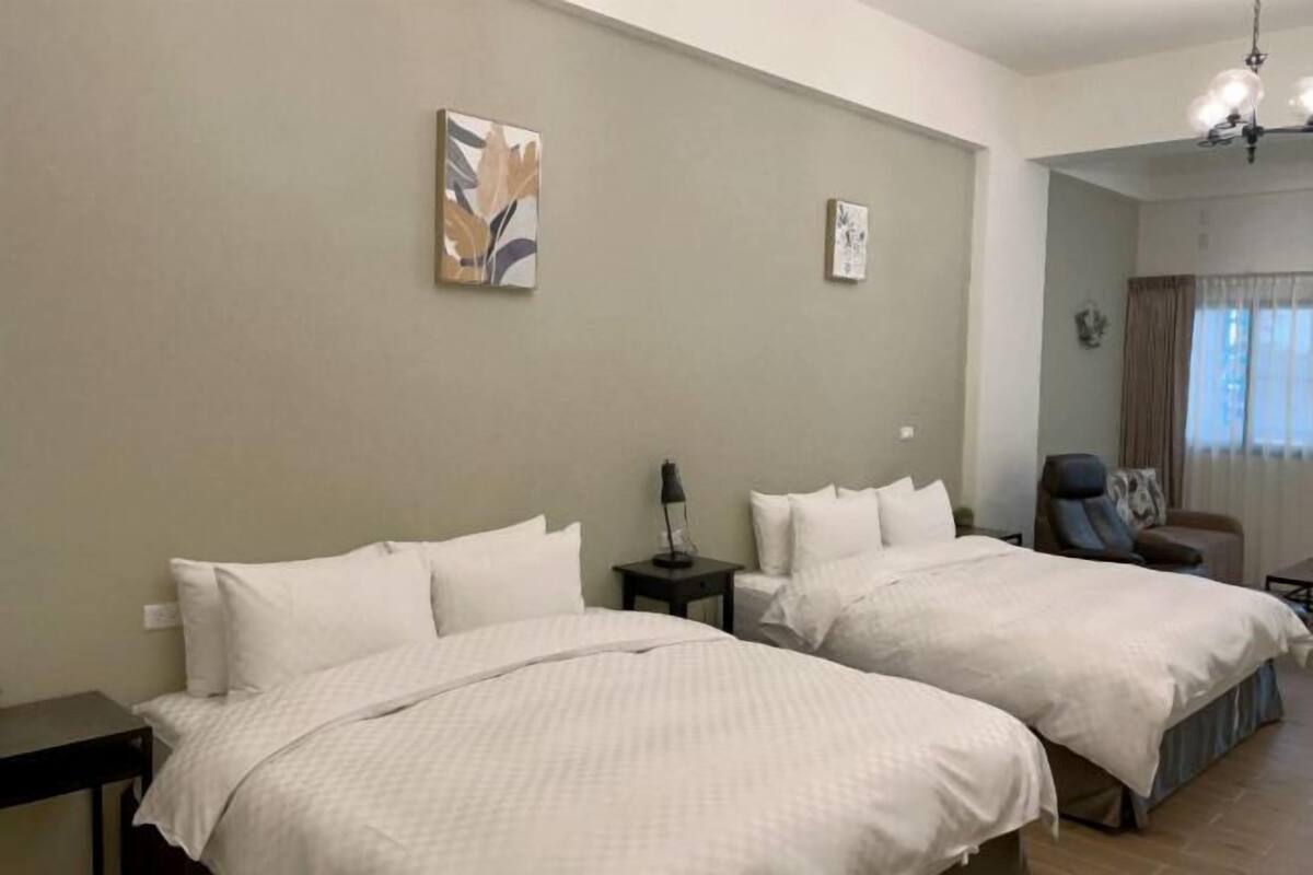 A hotel room with two beds, a desk, a chair, and a small table.