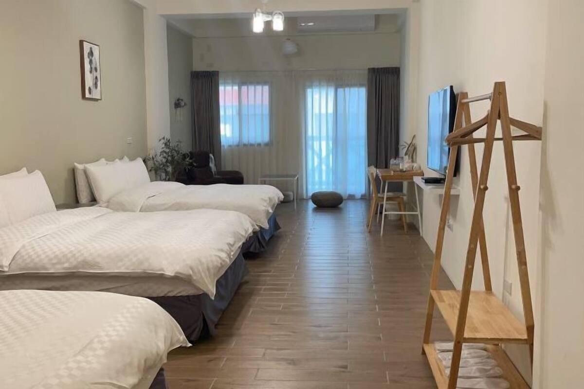 A hotel room with three beds, a wooden floor, a desk with a chair, and a television.