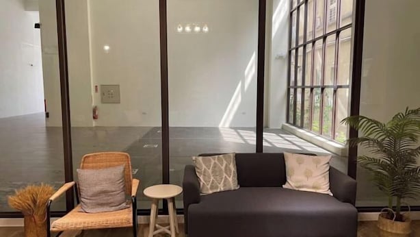 A modern living room with a dark sofa, a wicker chair, a small round table, and a potted plant. - Chju Inn (Tainan)