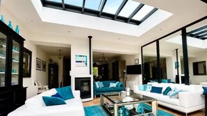 A modern living room with a skylight, white sofas, a glass coffee table, and teal cushions.