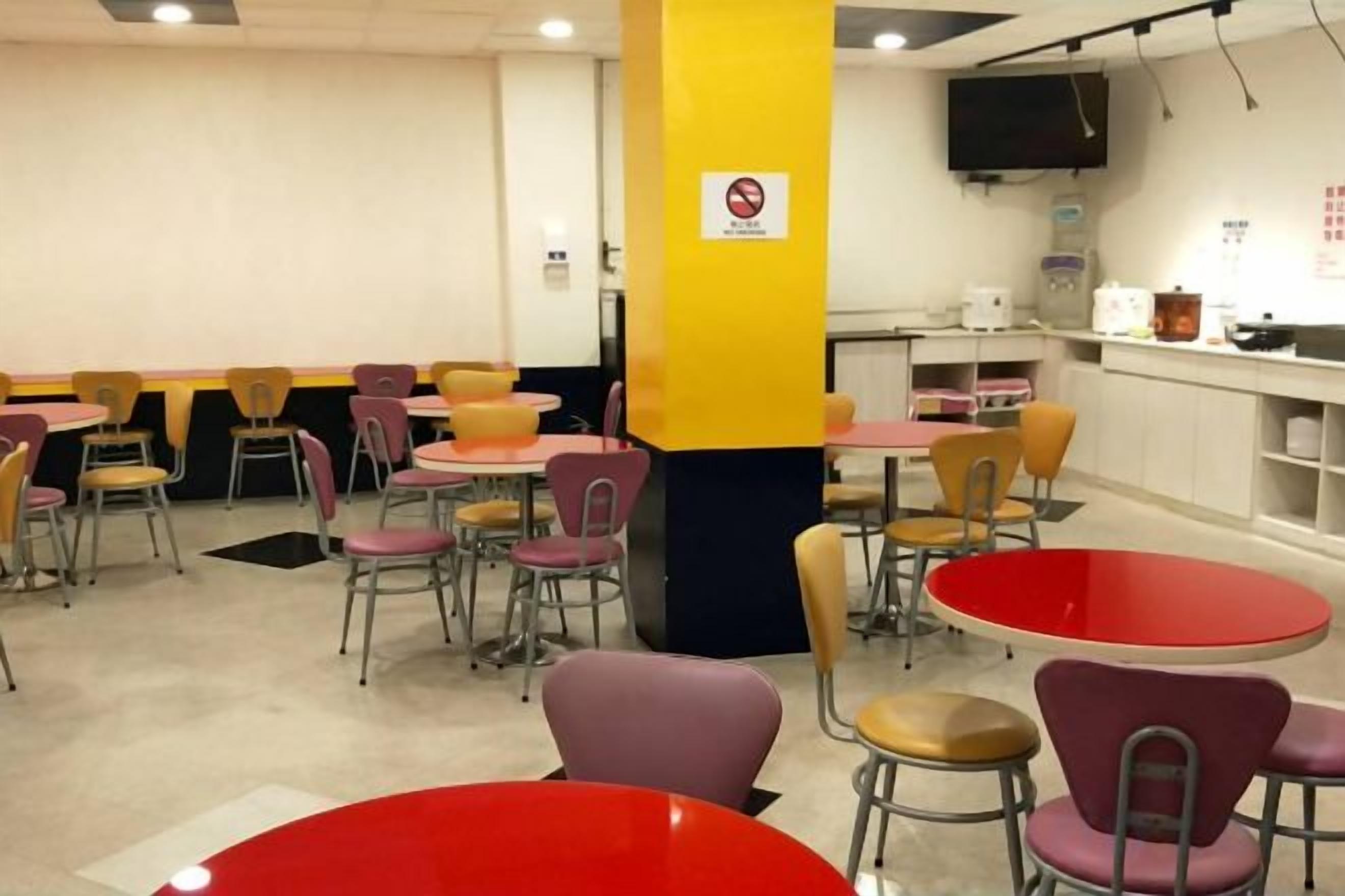 A cafeteria with round tables and chairs, a pillar with a no-smoking sign, and a television mounted on the wall.