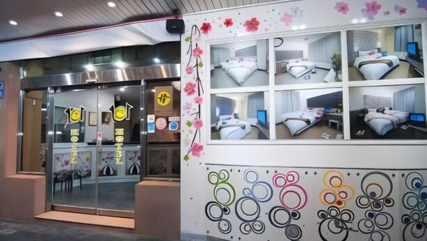 A hotel entrance with a glass door, a reception desk, and a wall with multiple rooms displayed. - 101 Hotel (Hsinchu)