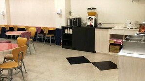 A dining area with round tables and chairs, a coffee station, and a flat-screen TV mounted on the wall. - 101 Hotel (Hsinchu)