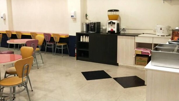 A dining area with round tables and chairs, a coffee station, and a flat-screen TV mounted on the wall. - 101 Hotel (Hsinchu)