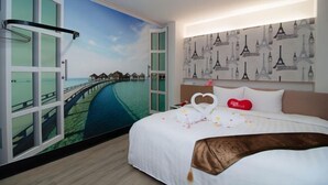 A hotel room with a large window, a bed with a white bedspread, a heart-shaped pillow, and a wall with a Paris-themed wallpaper. - 101 Hotel (Hsinchu)