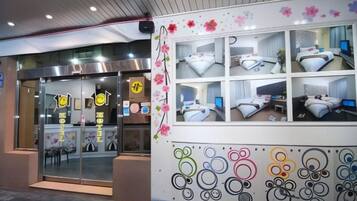 A hotel entrance with a reception desk, glass doors, and a wall with multiple rooms displayed.