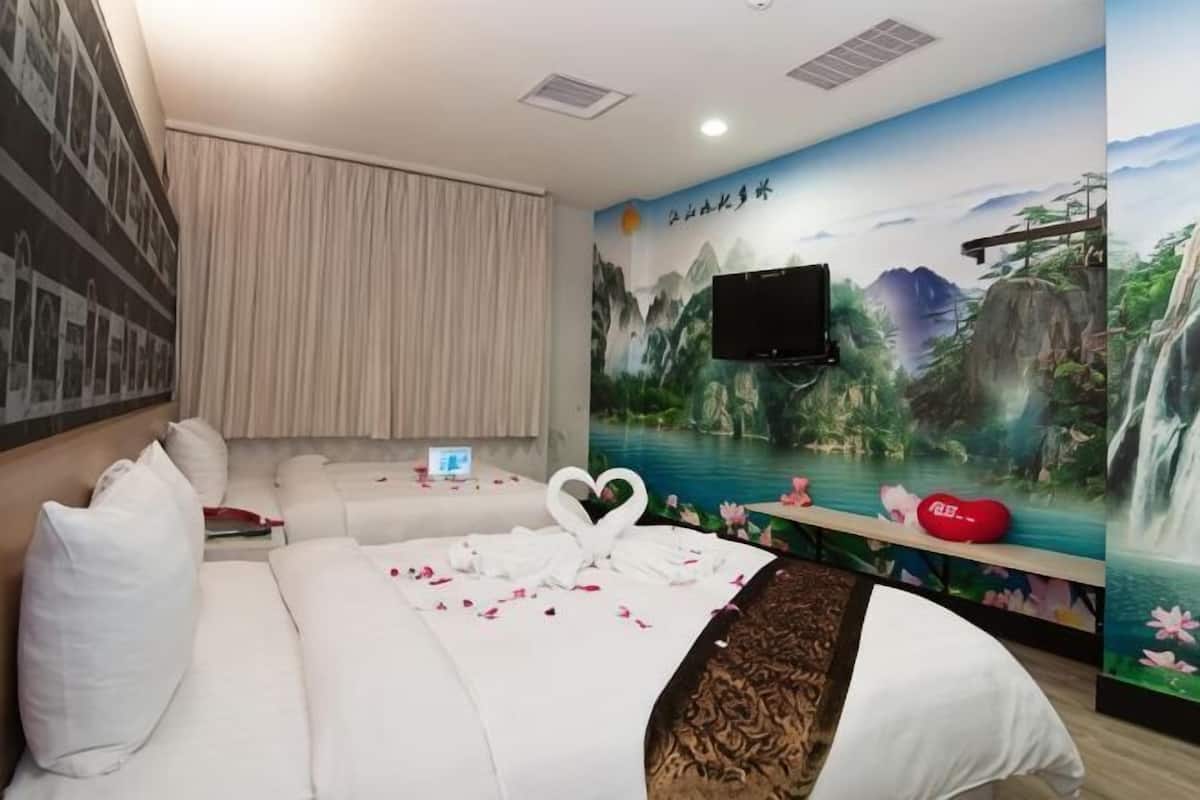 A hotel room with a bed, a sofa, a TV, and a mural of a mountainous landscape.