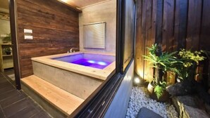 A spa area with a wooden wall, a hot tub, and a window with blinds. - Soundwater (Miaoli)