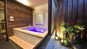 Zona de spa con pared de madera, jacuzzi y ventana con persianas.