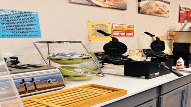 Una barra de desayuno con máquinas para gofres, una estación de café y diversas opciones de alimentos.