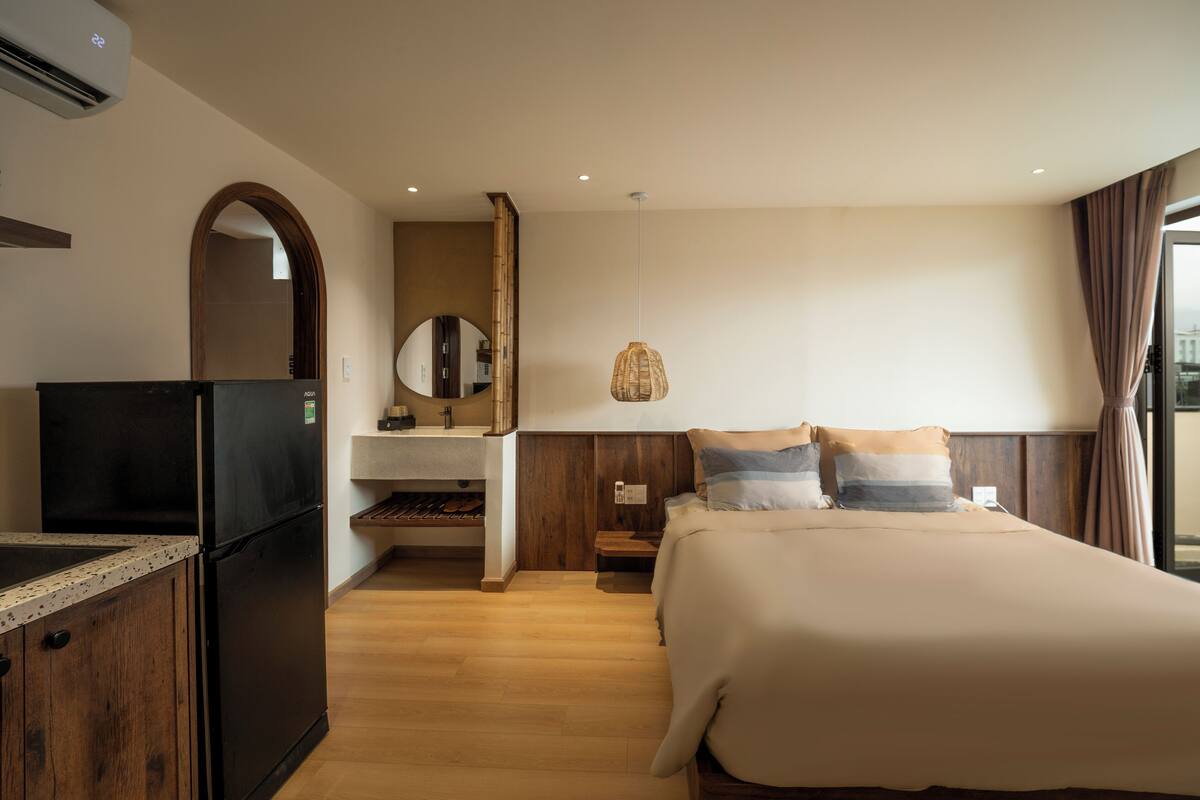 A hotel room with a bed, a TV, a minibar, a mirror, and a window with curtains.