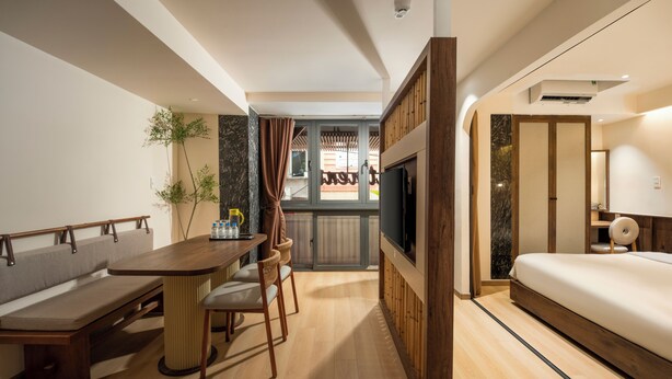 A modern hotel room with a wooden dining table, a sofa, a bed, and a TV. - Lune Boutique Hotel & Apartment Da nang (Da Nang)