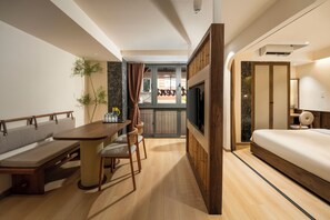 Ett modernt hotellrum med ett matbord i trä, en soffa, en säng och en TV.