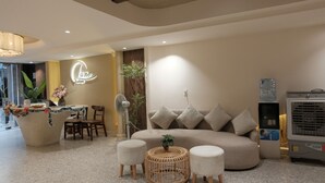 A modern hotel lobby with a reception desk, a sofa, two ottomans, a fan, and a water dispenser. - Lune Boutique Hotel & Apartment Da nang (Da Nang)