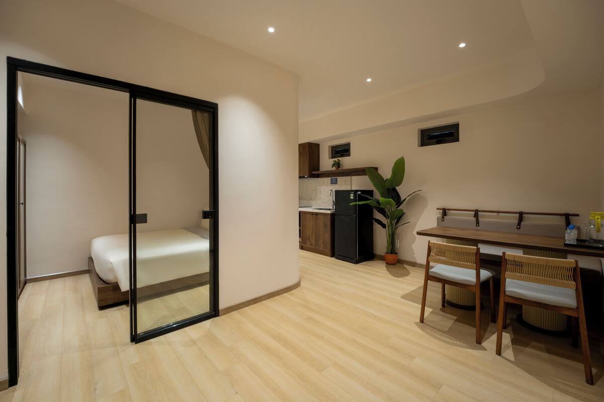 A modern room with a bed, a dining area with chairs, a kitchen with a refrigerator, and a potted plant.