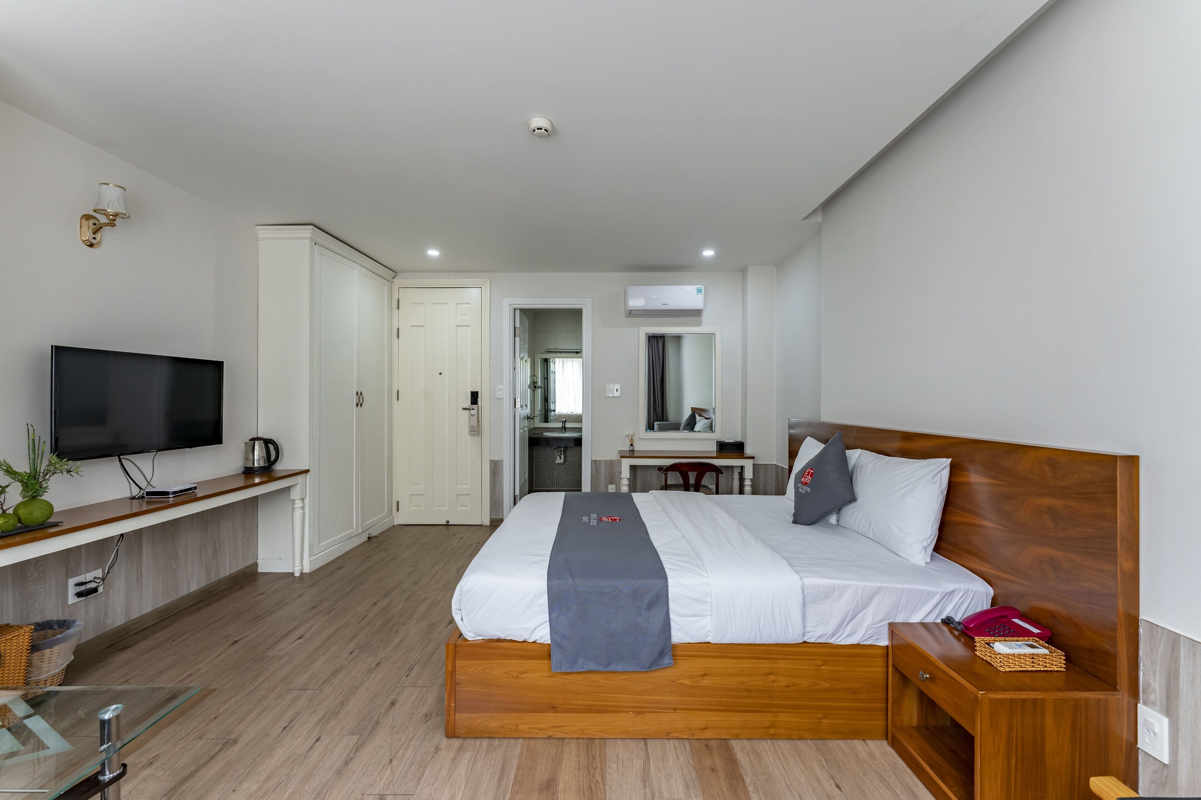 Quarto de hotel moderno com uma cama grande, televisão, escrivaninha e banheiro visível por uma porta aberta.