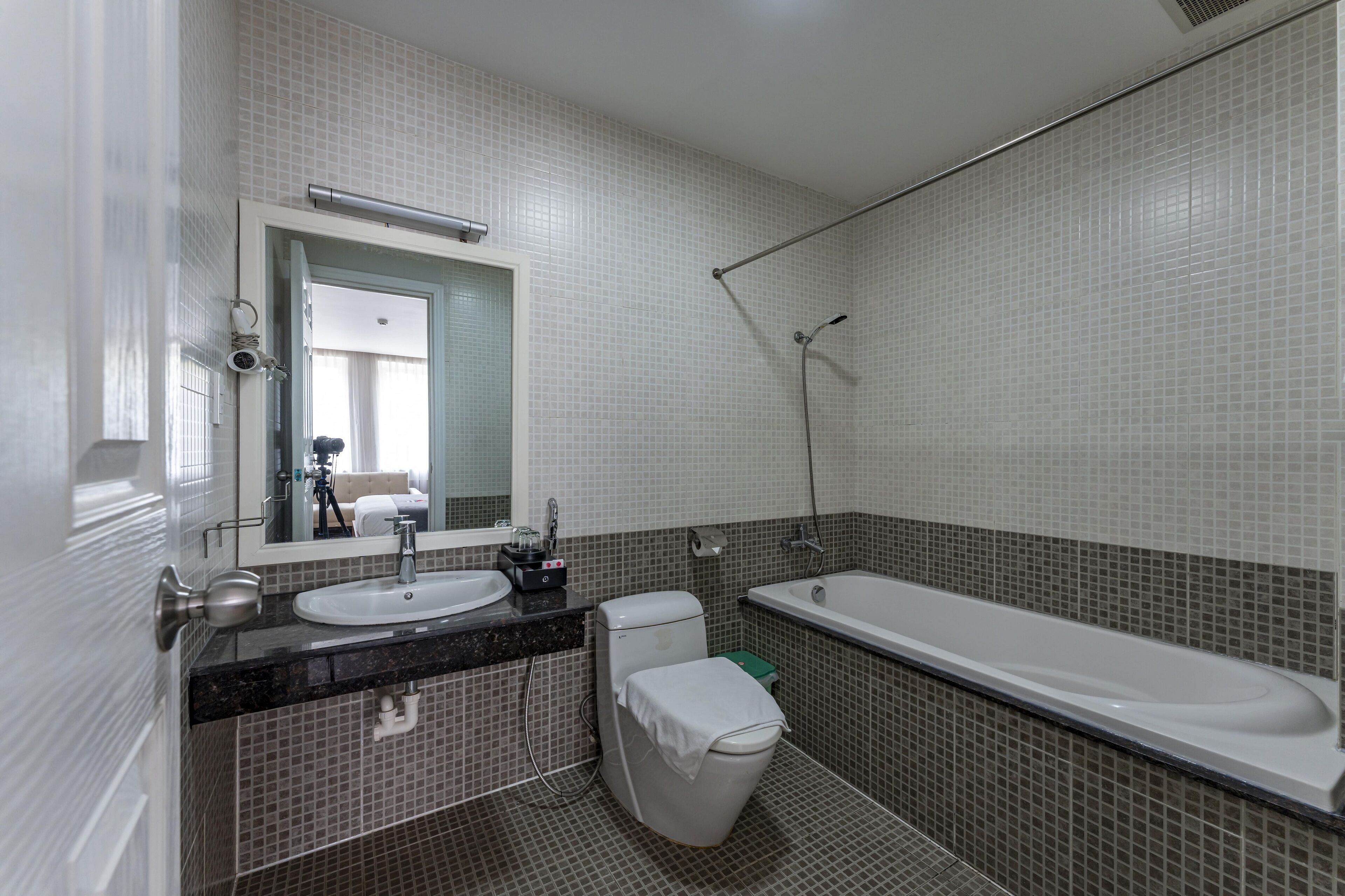 Ein modernes Badezimmer mit Waschbecken, Toilette und Badewanne, mit gefliesten Wänden und einem Spiegel über dem Waschbecken.