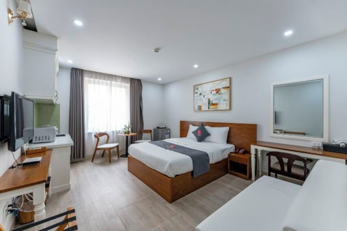 A hotel room with a bed, bedside table, desk, chair, and a television.