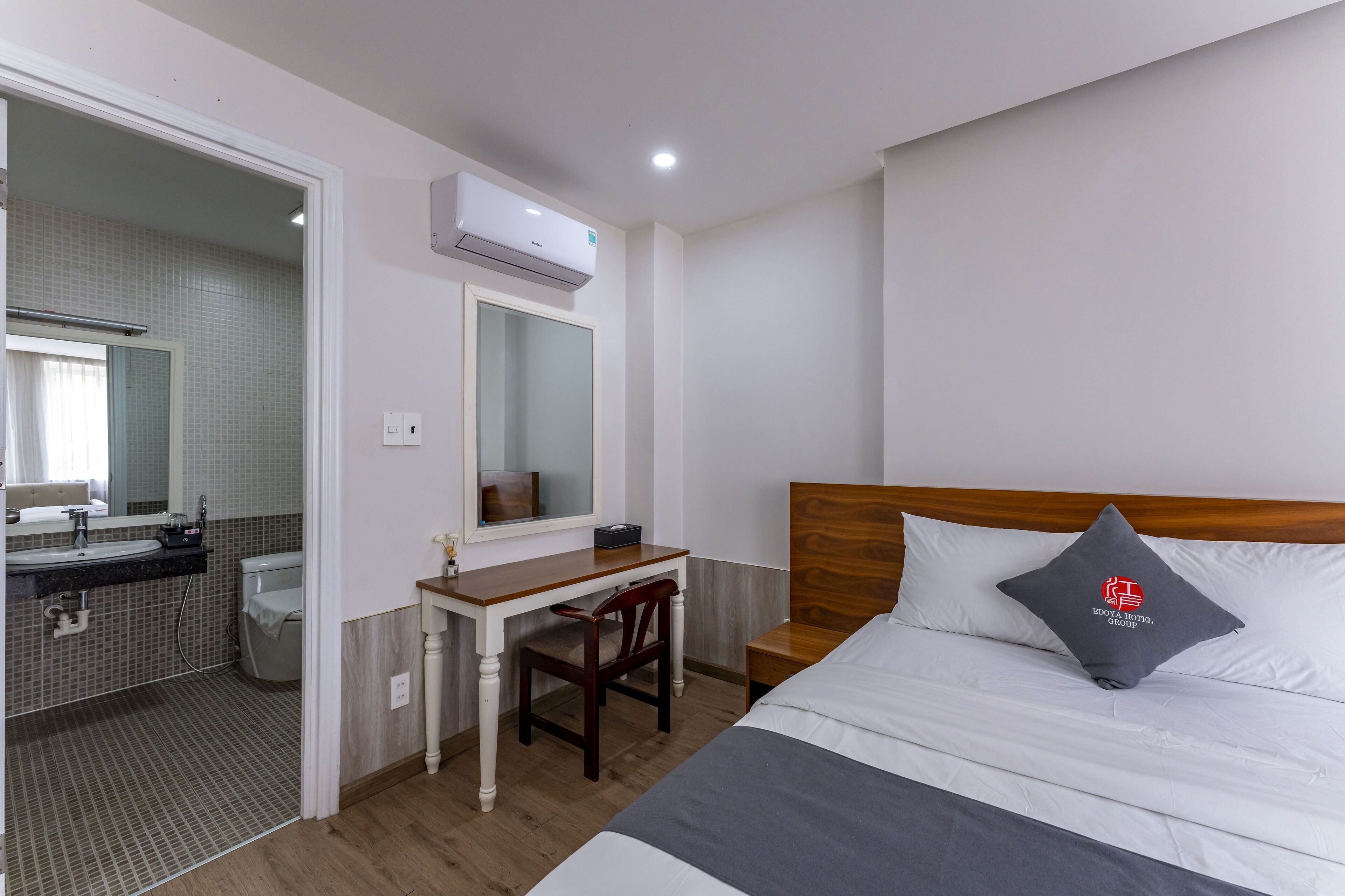 Una habitación de hotel con cama, escritorio, silla, espejo, inodoro y unidad de aire acondicionado.