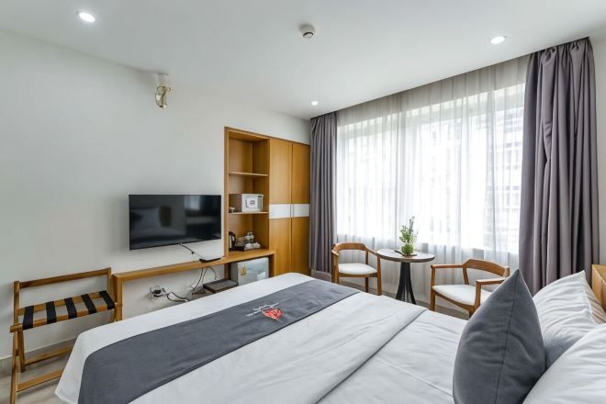 A hotel room with a bed, a TV, a desk with a chair, and a small table with a plant.