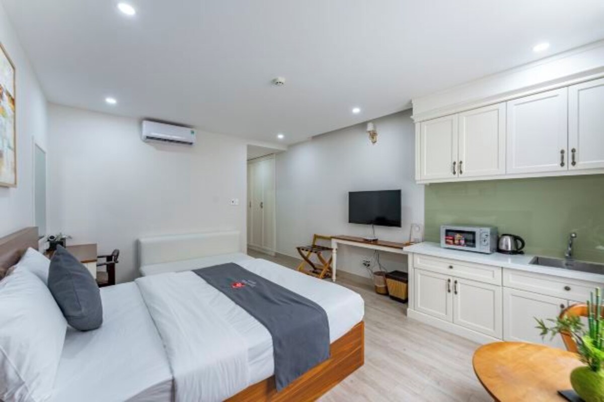A hotel room with a bed, a desk, a TV, and a kitchenette.
