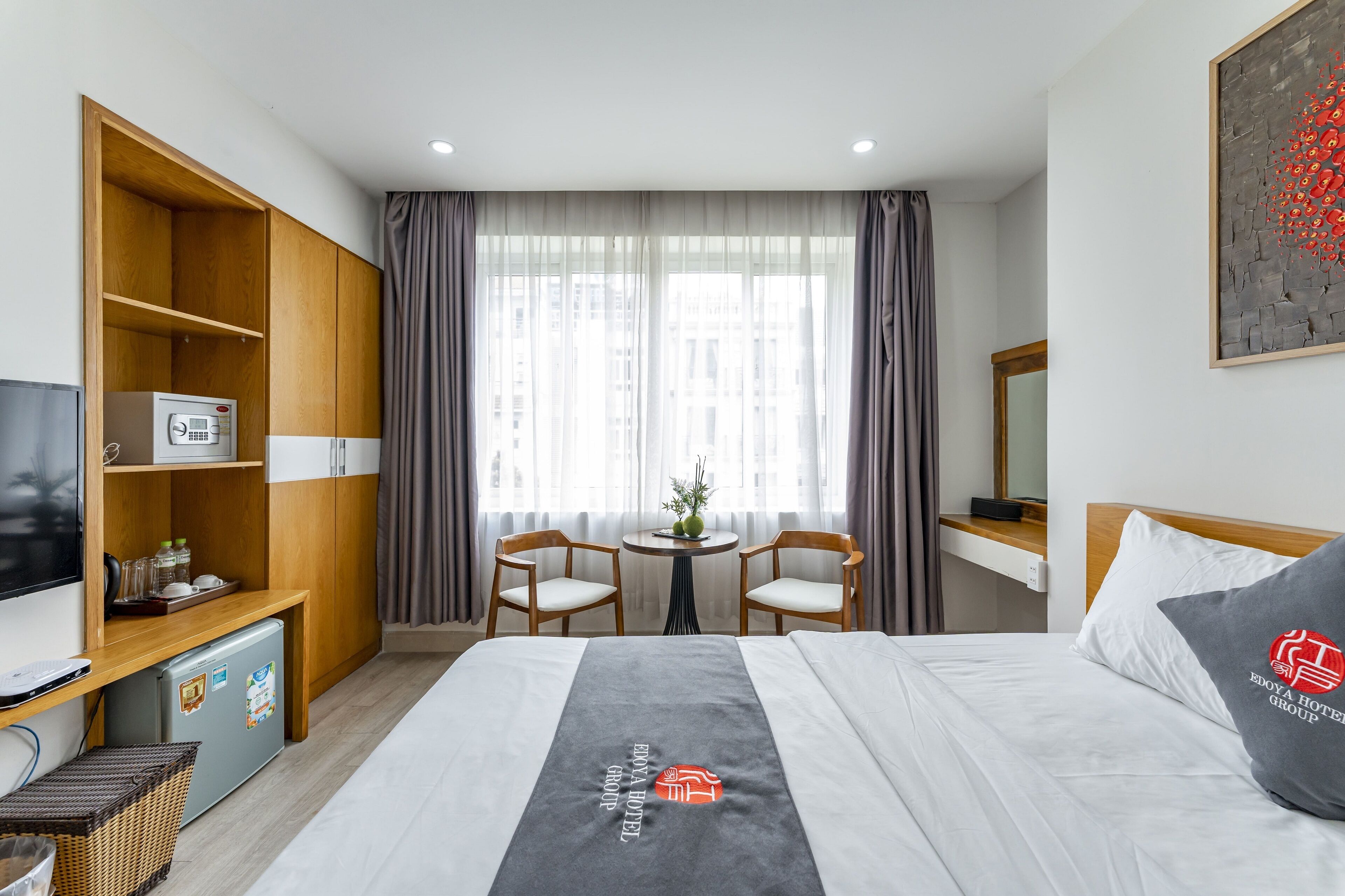 Habitación de hotel con cama, escritorio con computadora, refrigerador pequeño, televisión y ventana con cortinas.