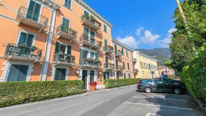 A row of multi-story buildings with balconies, a parked car, and a clear blue sky. - Bogliaco Lake Front, Gargnano, Italy (Gargnano)