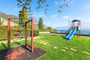 Un parque infantil con tobogán y estructura para escalar, con montañas y una masa de agua de fondo.