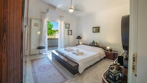 A bedroom with a bed, a nightstand, a lamp, a radio, a window with curtains, and a view of greenery outside. - Villa Calò 2 with Garden, 200 meters from Sea, Maruggio, Italy (Maruggio)