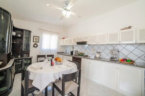 Un comedor con una mesa redonda, sillas, ventilador de techo y armarios de cocina.