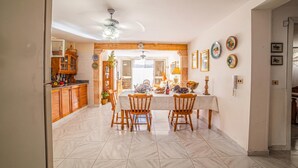 Uma área de refeições com mesa, cadeiras e cozinha ao fundo.