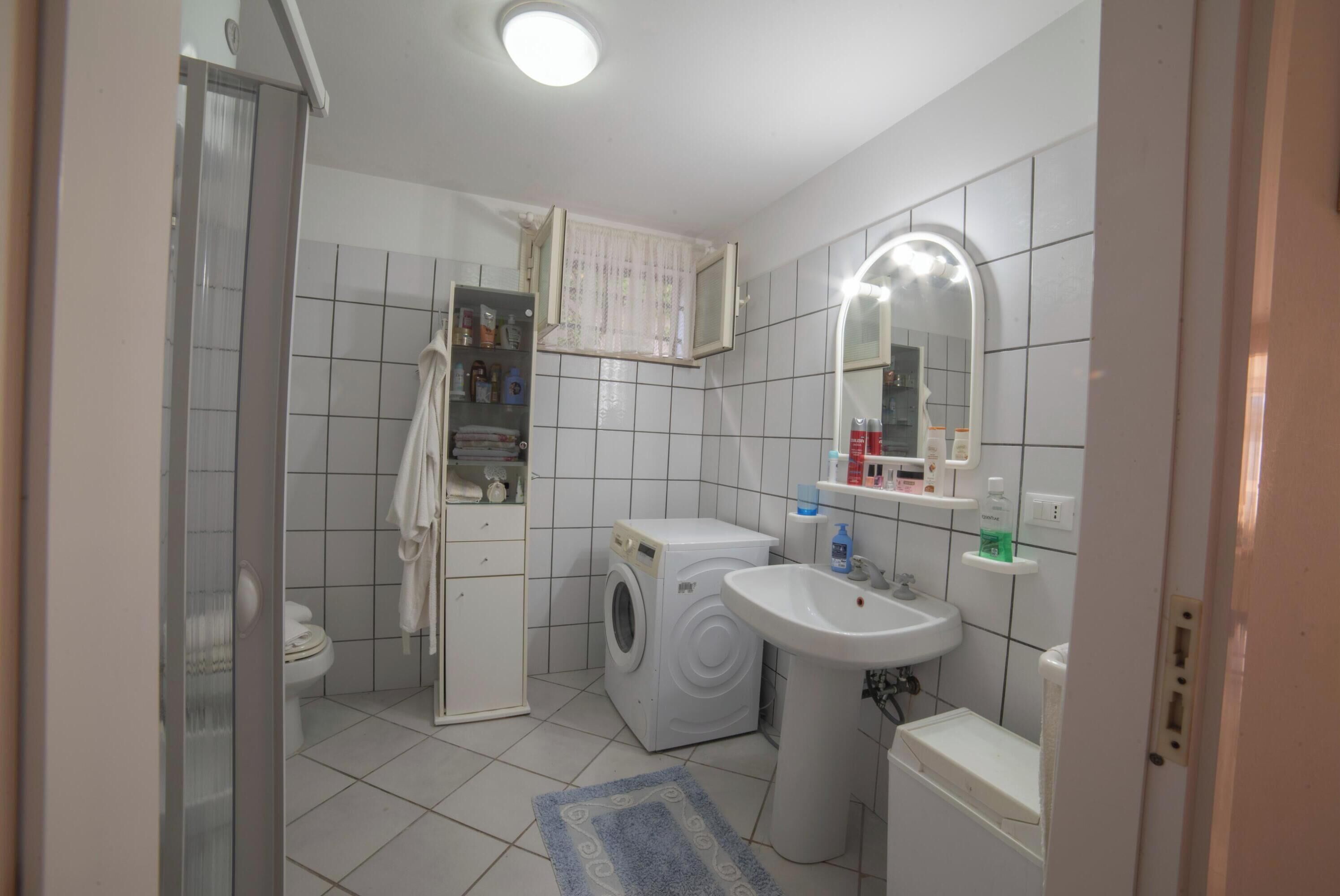 Une petite salle de bain propre, équipée de toilettes, d’un lave-linge, d’un lavabo et d’un miroir.
