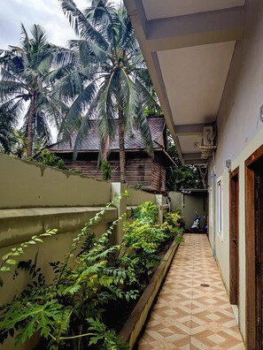 A narrow corridor with a tiled floor, a concrete wall on one side, and a wooden door on the other. - AHHA Residence Kampot (Kampot)