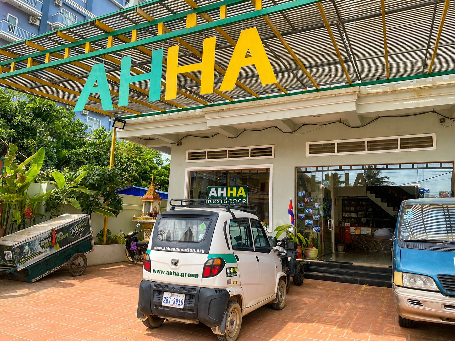 A building with a large sign reading 'AHHA Residence' and a parked vehicle in front.