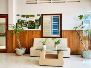 A reception area with a wooden wall, a bulletin board, a sofa, and two potted plants. - AHHA Residence Kampot (Kampot)