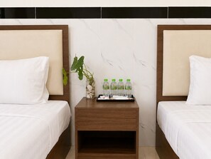 A hotel room with two beds, a nightstand with a plant and water bottles, and a marble wall. - AHHA Residence Kampot (Kampot)
